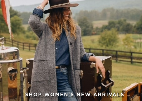 woman standing outside, leaning on steamer trunk, wearing denim shirt, cowboy hat and gray cardigan coat