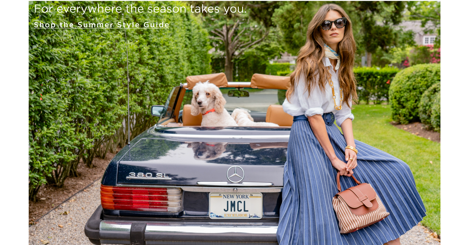 Woman seated on the top of a convertible, outside, wearing a navy pleated skirt with a white linen button down shirt tucked in