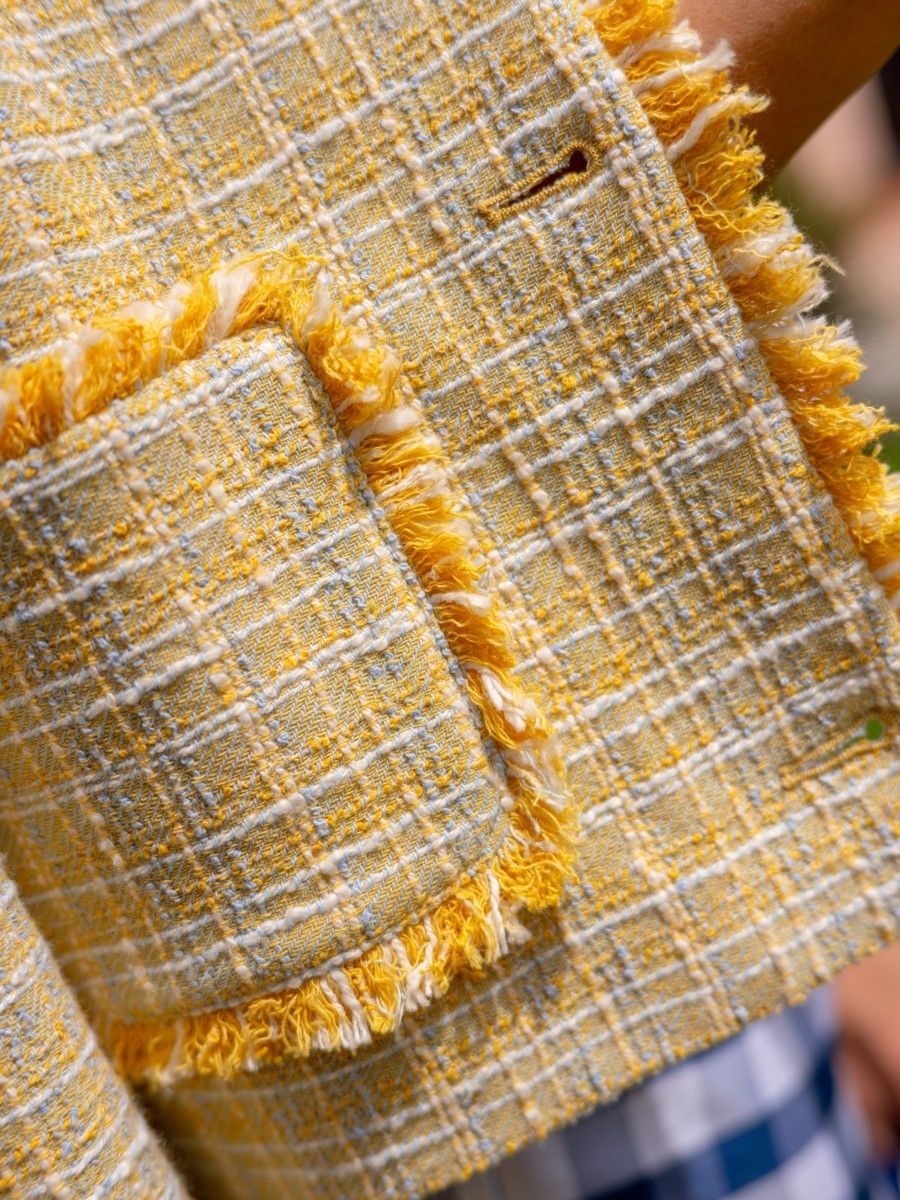 A yellow, white, and light blue tweed jacket with frayed edges and a buttonhole.