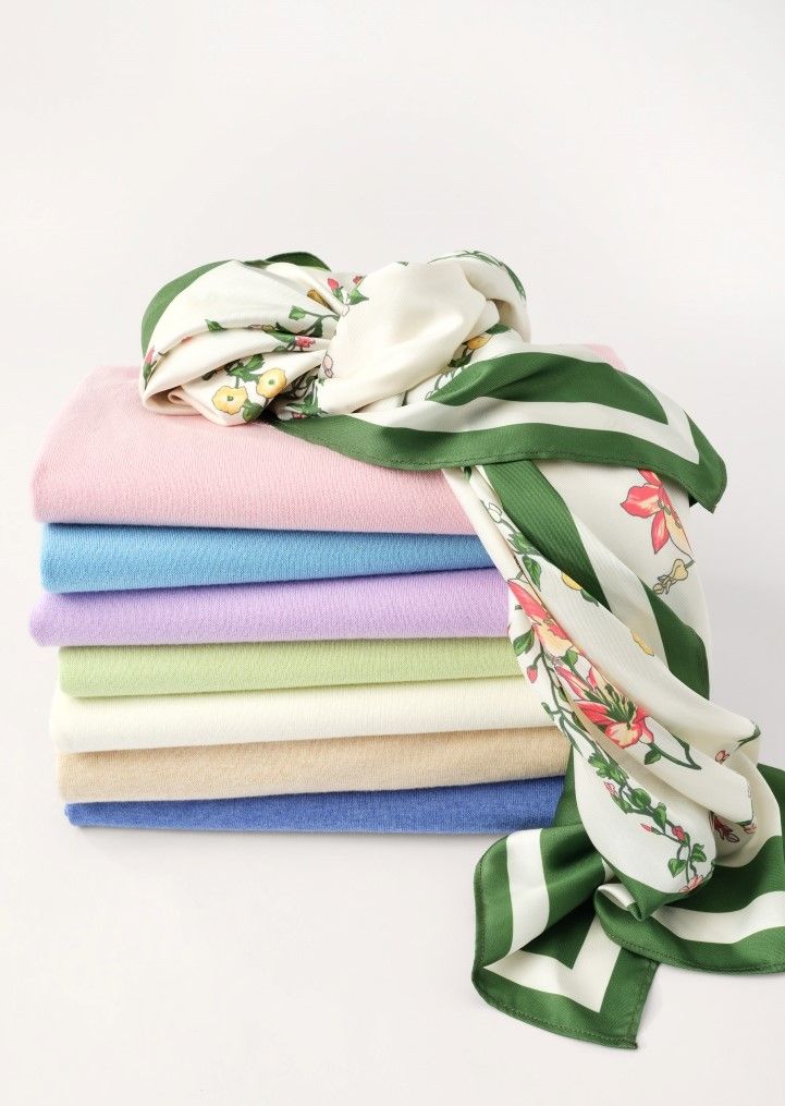 A stack of folded pastel sweaters topped with a white floral and green striped scarf.