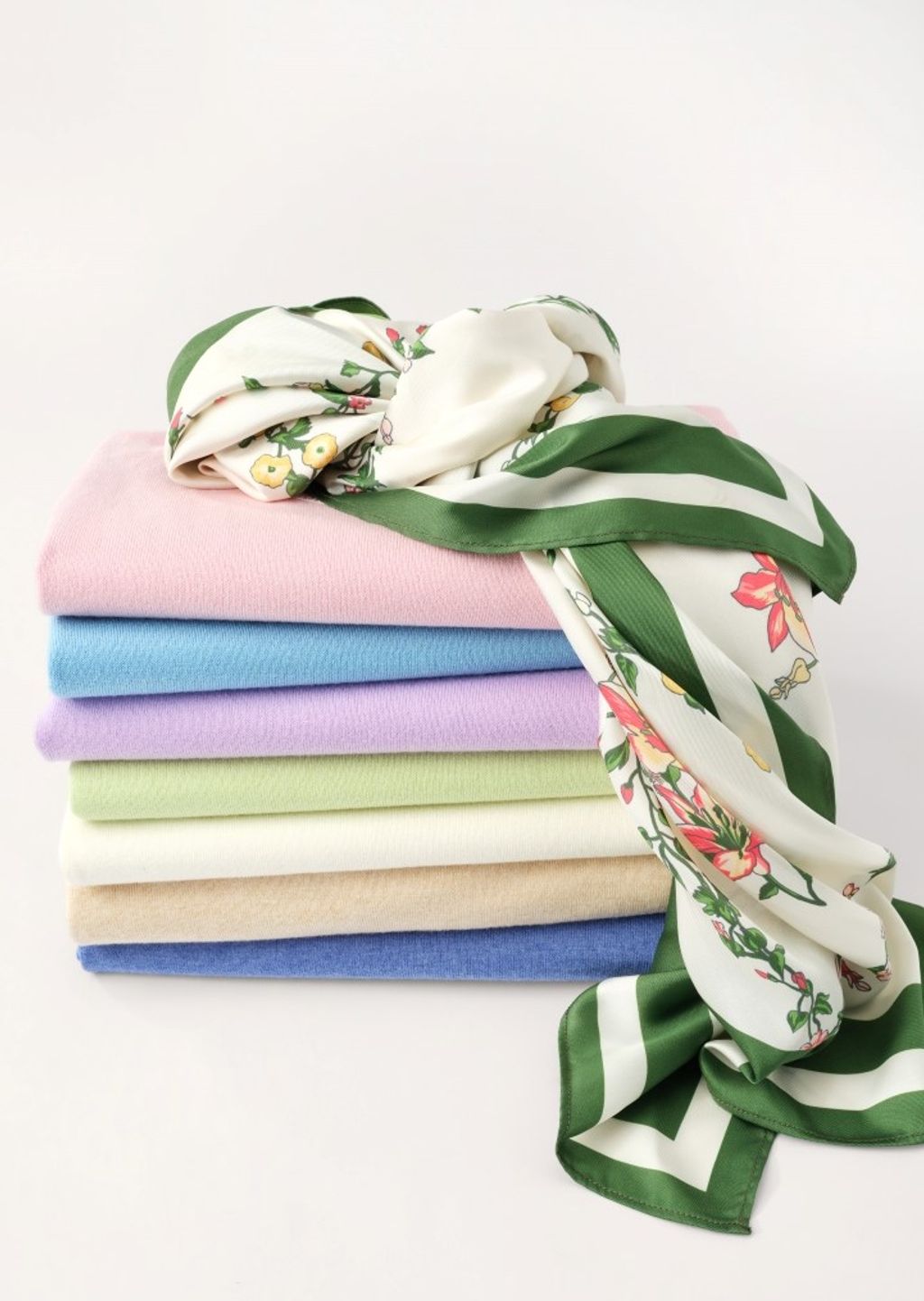 A stack of folded pastel sweaters topped with a white floral and green striped scarf.