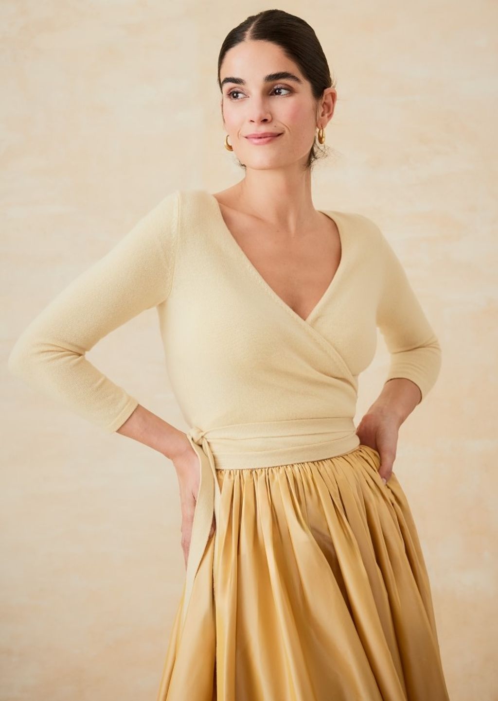woman standing with hands on hips wearing yellow wrap sweater