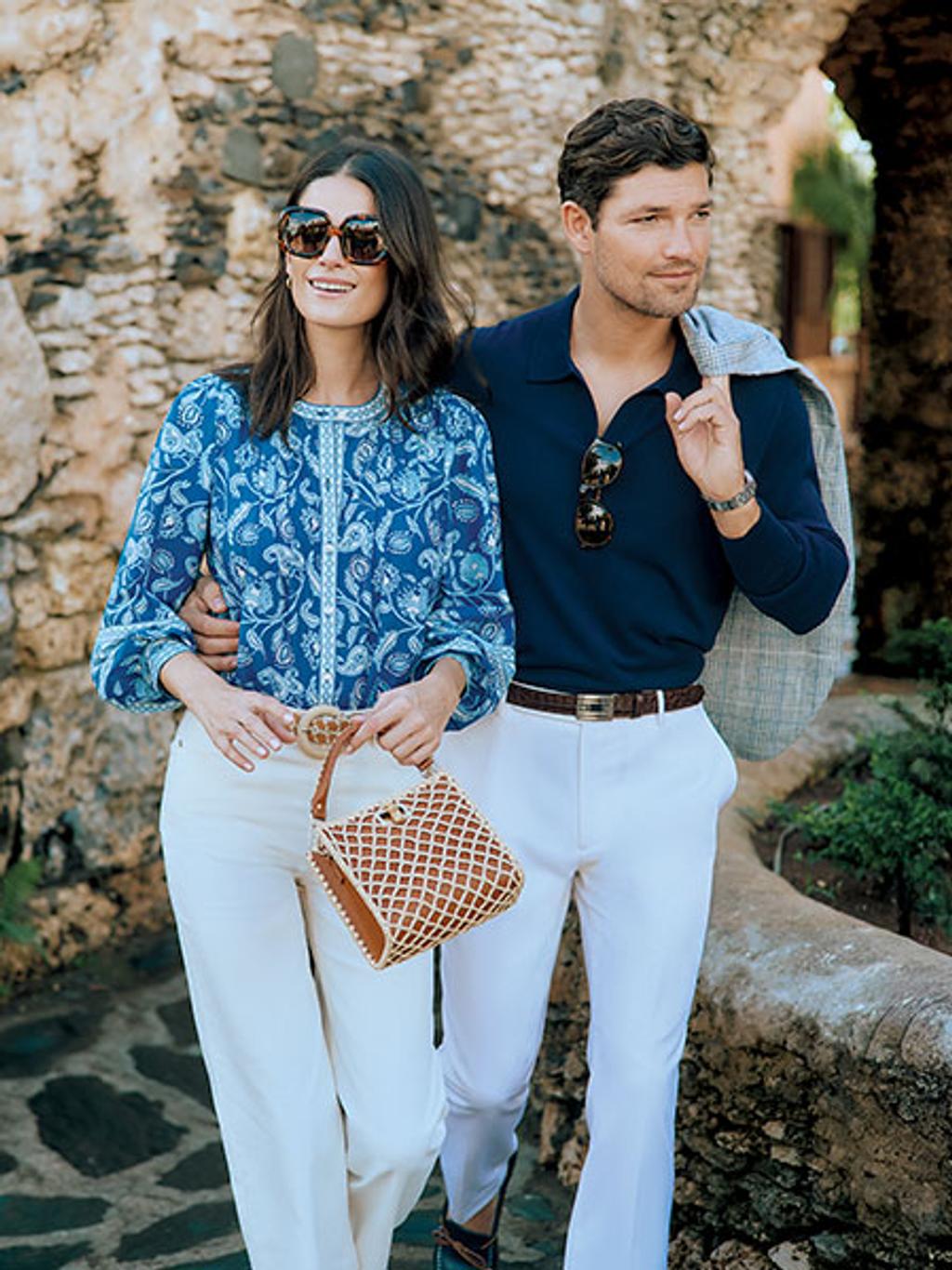 Model holding woven bag, wearing blue floral top and white jeans