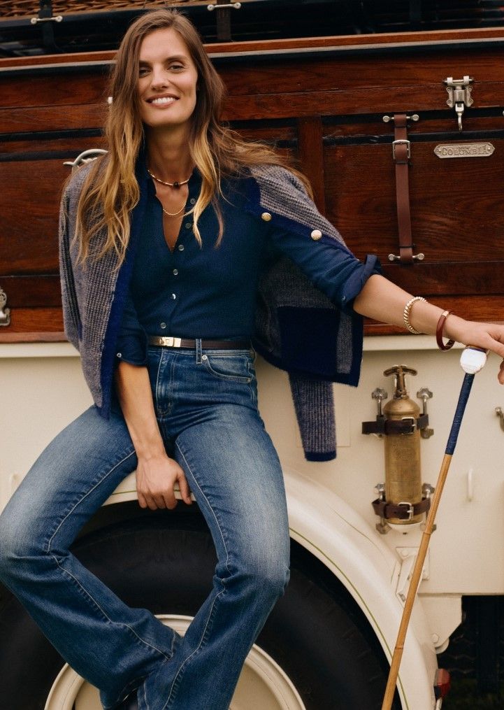 woman sitting on side of truck wearing medium wash denim jeans, navy ribbed button down knit shirt and navy textured cardigan over her shoulders