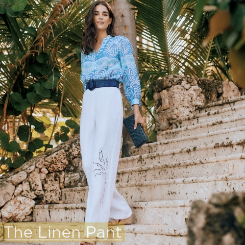 woman walking down stone steps with lush greens around her wearing white linen embroidered pants and blue puff sleeve geo pattern blouse