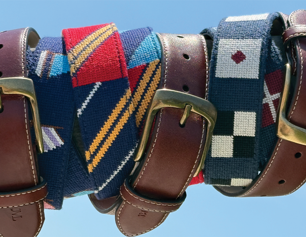A row of several belts, some leather with buckles and some fabric with nautical and striped patterns, against a blue sky.