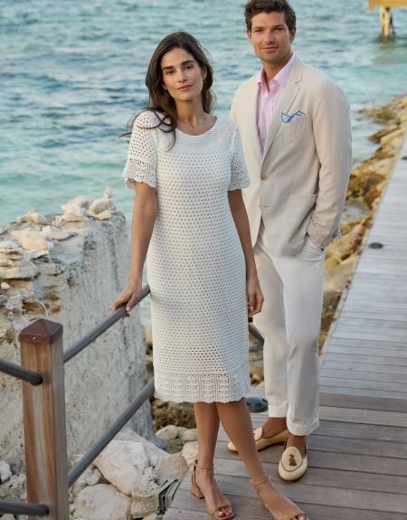 woman and man standing on beach deck in white crochet dress and linen respectively