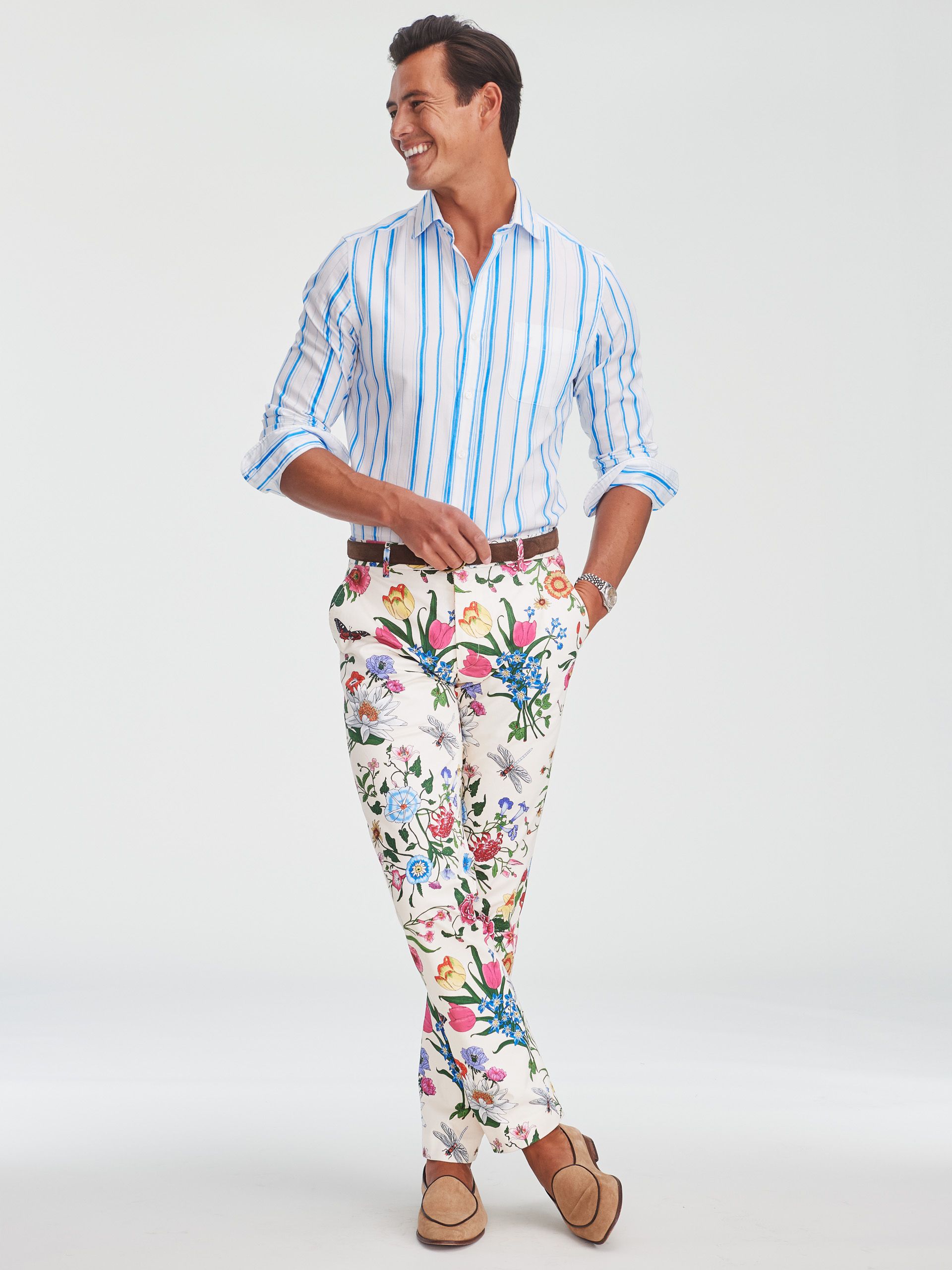 A smiling man in a blue and white striped shirt, colorful floral pants, and tan loafers.