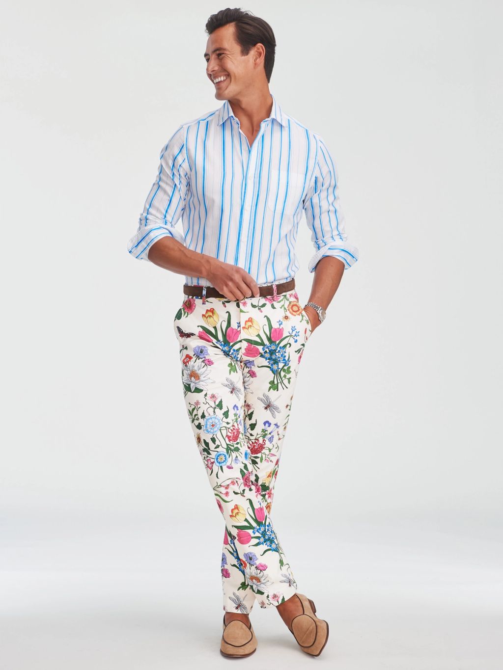 A smiling man in a blue and white striped shirt, colorful floral pants, and tan loafers.