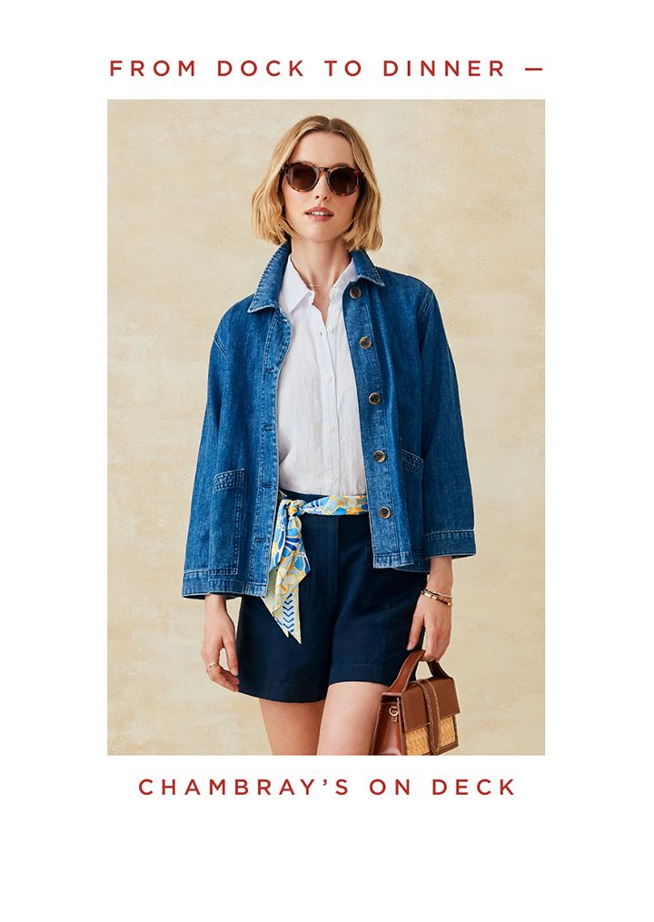 Woman standing in fisherman inspired denim jacket with navy linen shorts. 