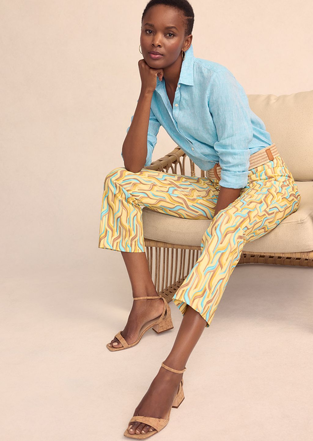 Model seated while wearing turquoise and brown patterned pants and blue linen shirt.