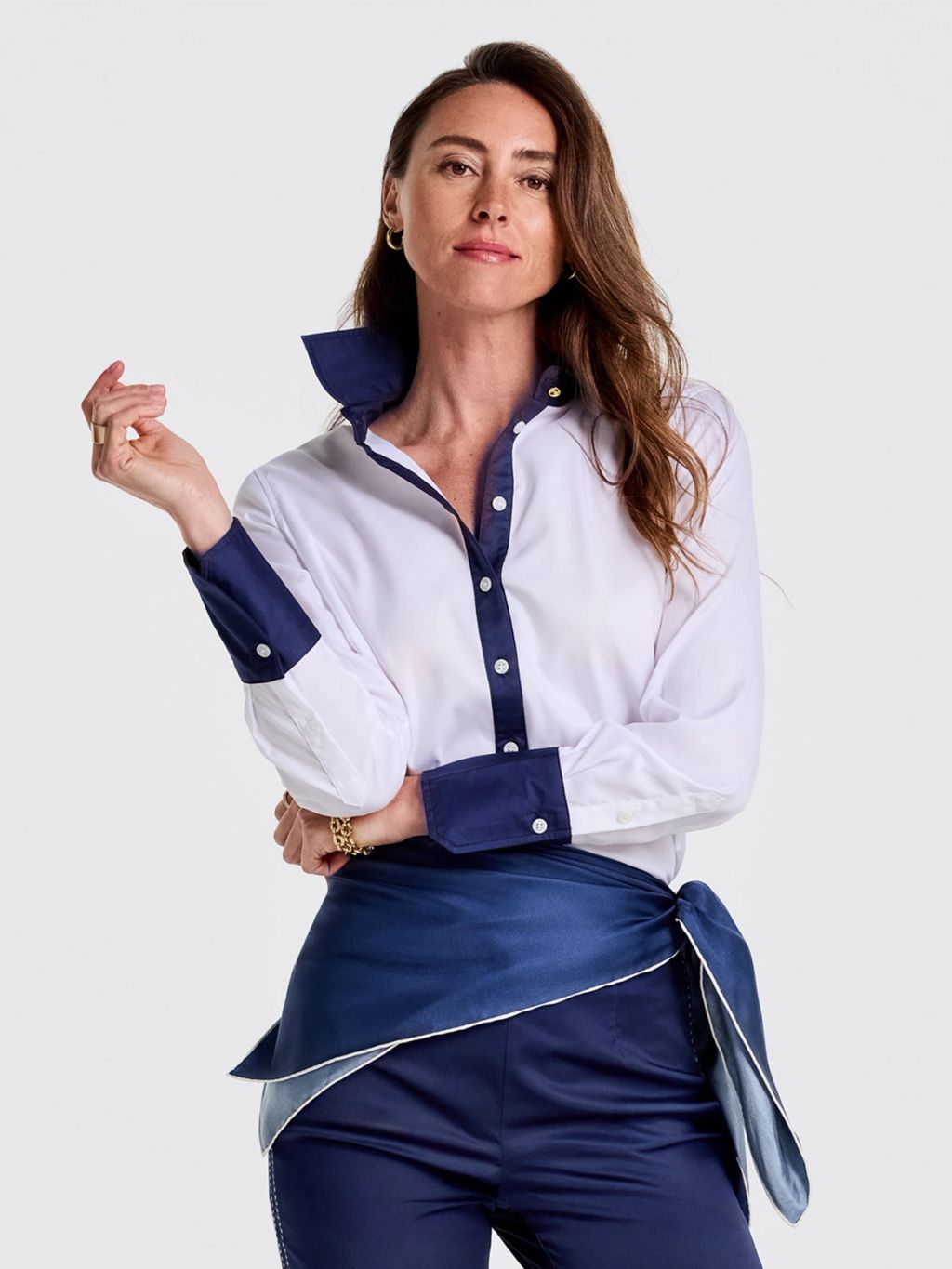 A woman in a white shirt with navy collar and cuffs, navy trousers, and a tied navy satin sash.