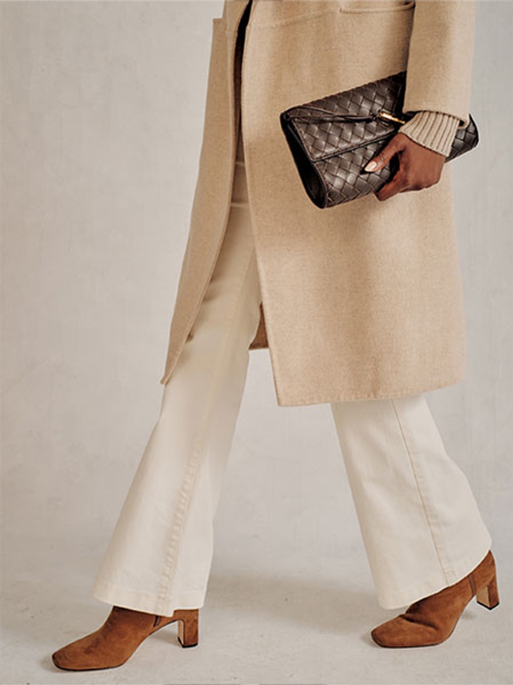 Model in a coat and jeans carrying a woven clutch Model in a coat and jeans carrying a woven clutch