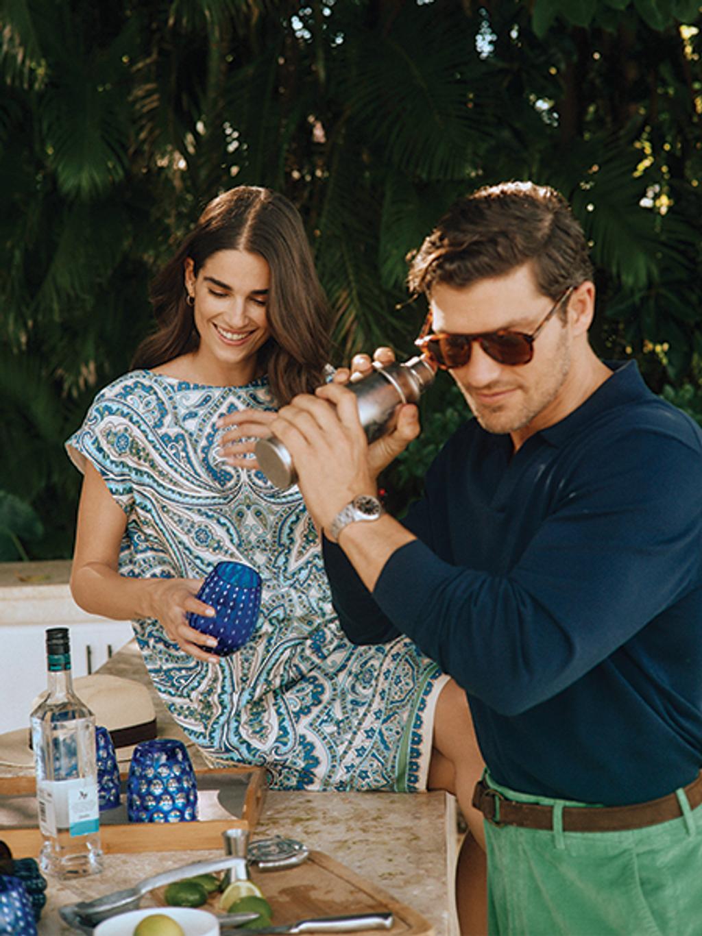 Male model making a margarita. Female model sitting with glass.