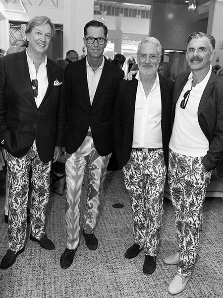 Black and white photo of four men in dark blazers and patterned trousers standing together.