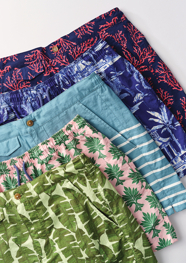 Five pairs of colorful tropical-patterned shorts arranged diagonally.