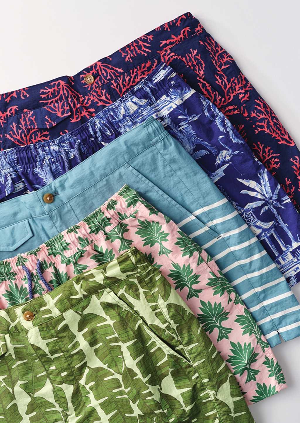 Five pairs of colorful tropical-patterned shorts arranged diagonally.