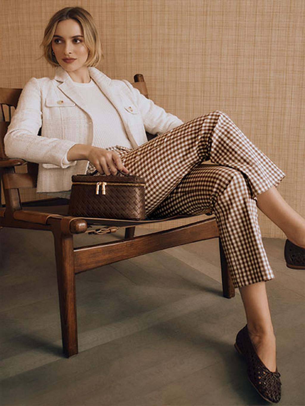 Women sitting in a chair wearing a white blazer and brown gingham pants.