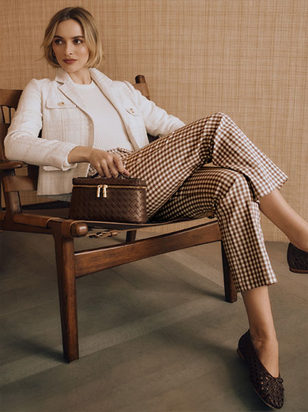 Women sitting in a chair wearing a white blazer and brown gingham pants.