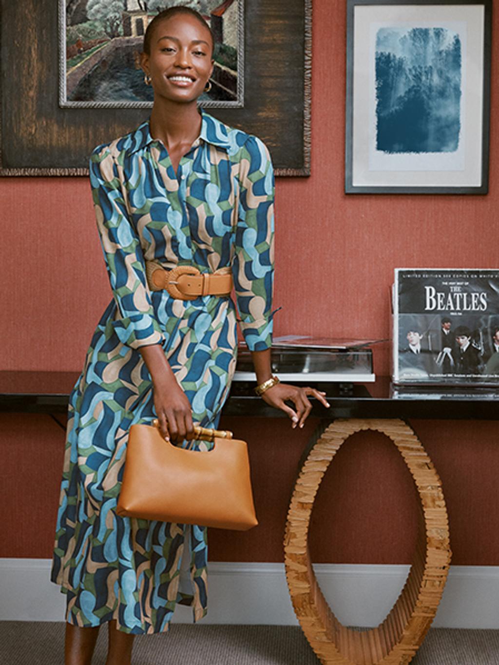 Model wearing printed midi dress with woven leather belt and leather and bamboo bag.