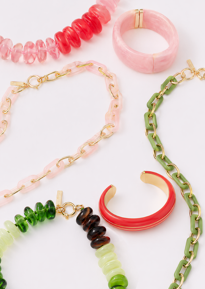 A flat lay of colorful resin and gold jewelry, including necklaces, bracelets, and bangles, in shades of pink, red, and green.