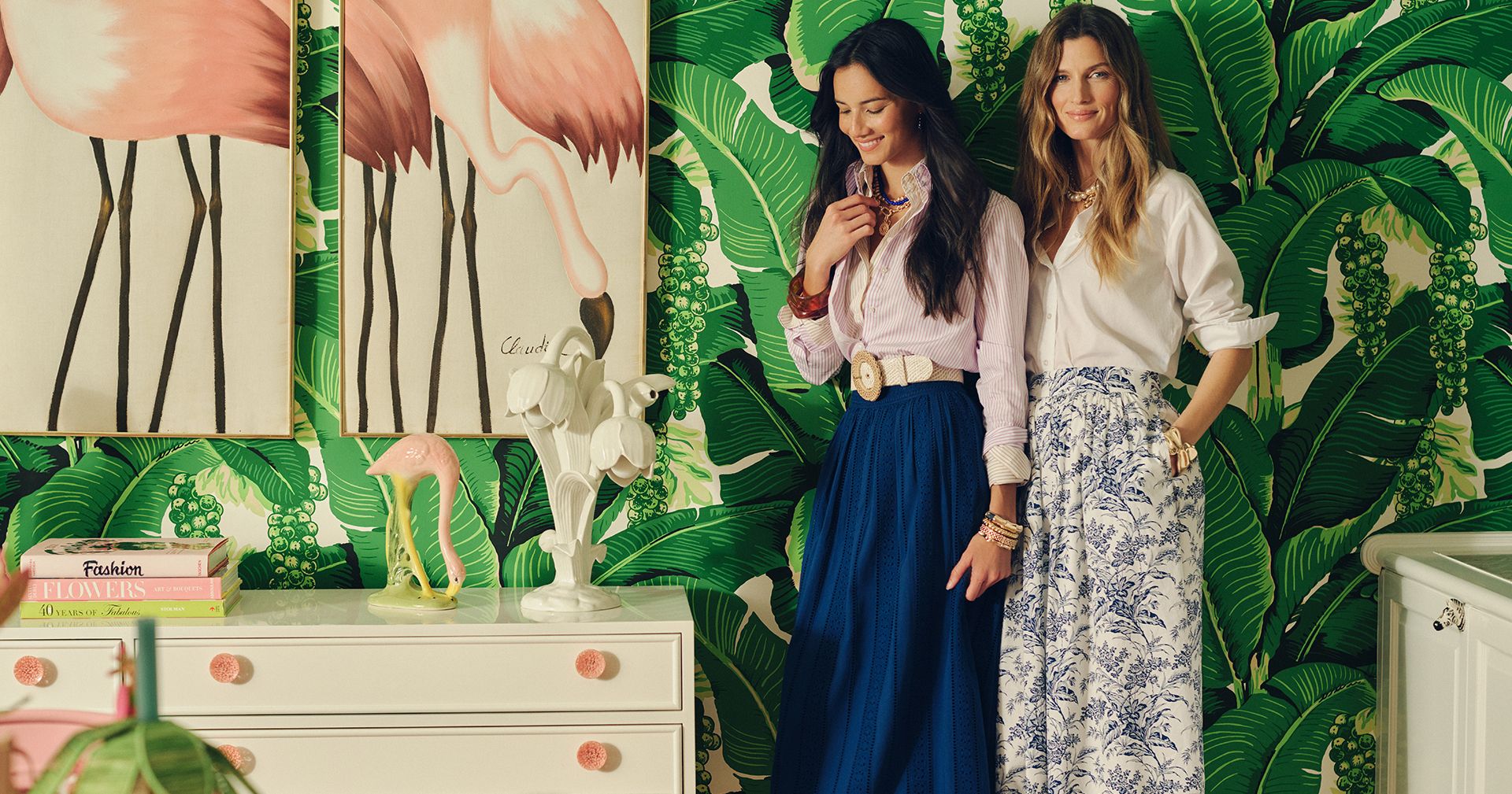 group of women walking standing against a palm tree printed wall wearing cotton midi skirts and button down shirts.
