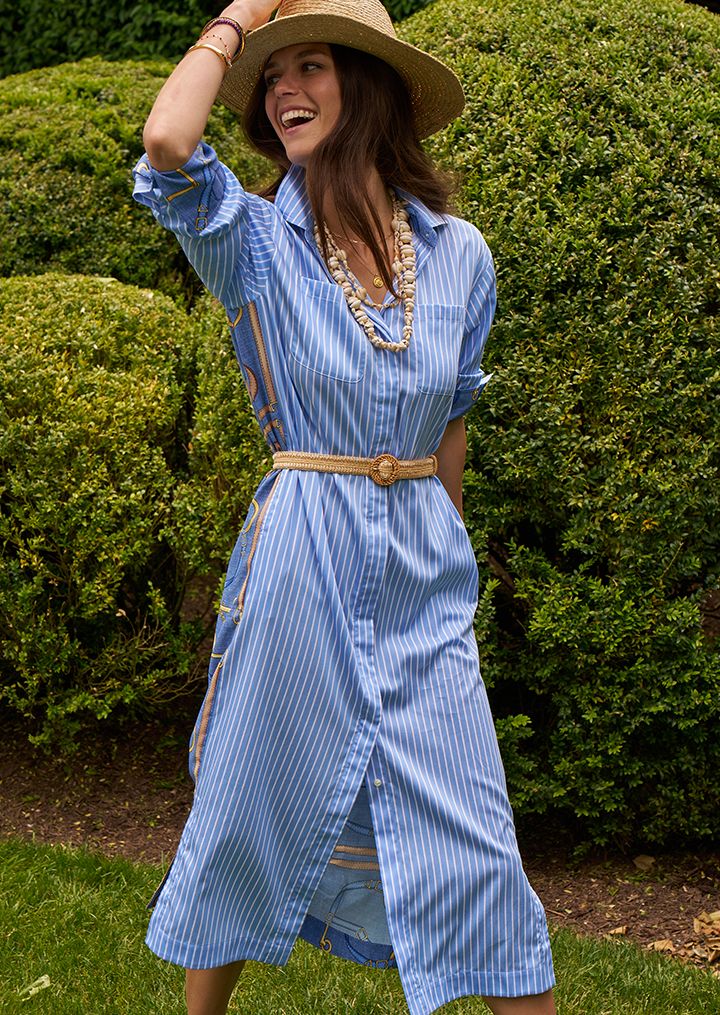 Woman standing in a blue and white striped dressing holding the hat on her head