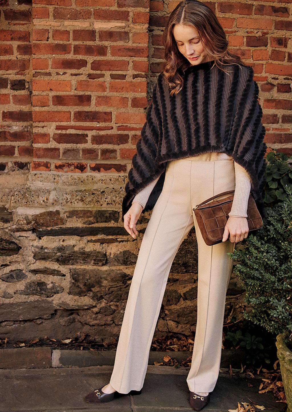 Woman wearing a brown faux fur poncho, beige sweater, beige pants, and brown pumps.