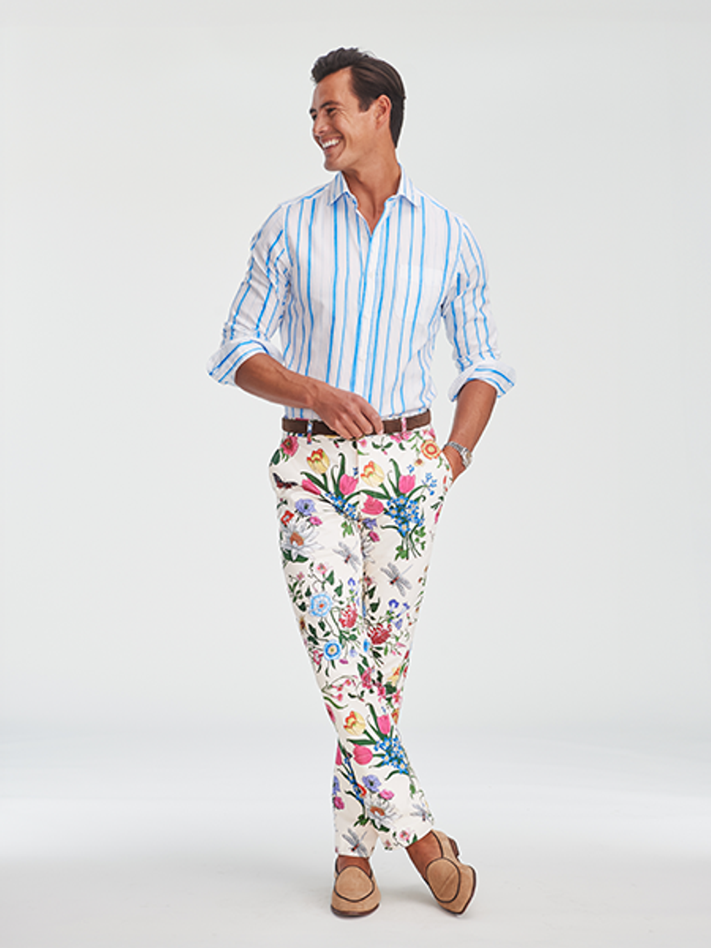 A smiling man in a blue and white striped shirt, white floral pants, and tan loafers.