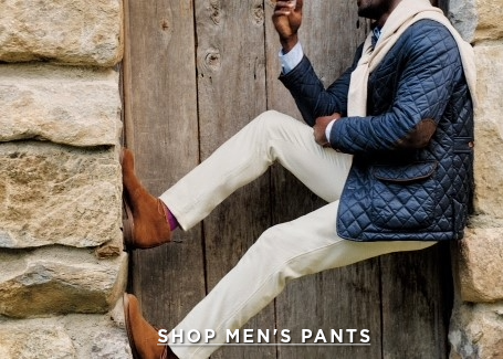 man positioned in stone doorway with light khaki pants on and suede boots propping him up