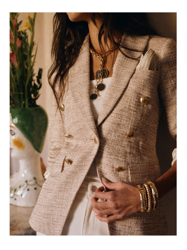 close up image of woman wearing tan double breasted blazer with gold buttons