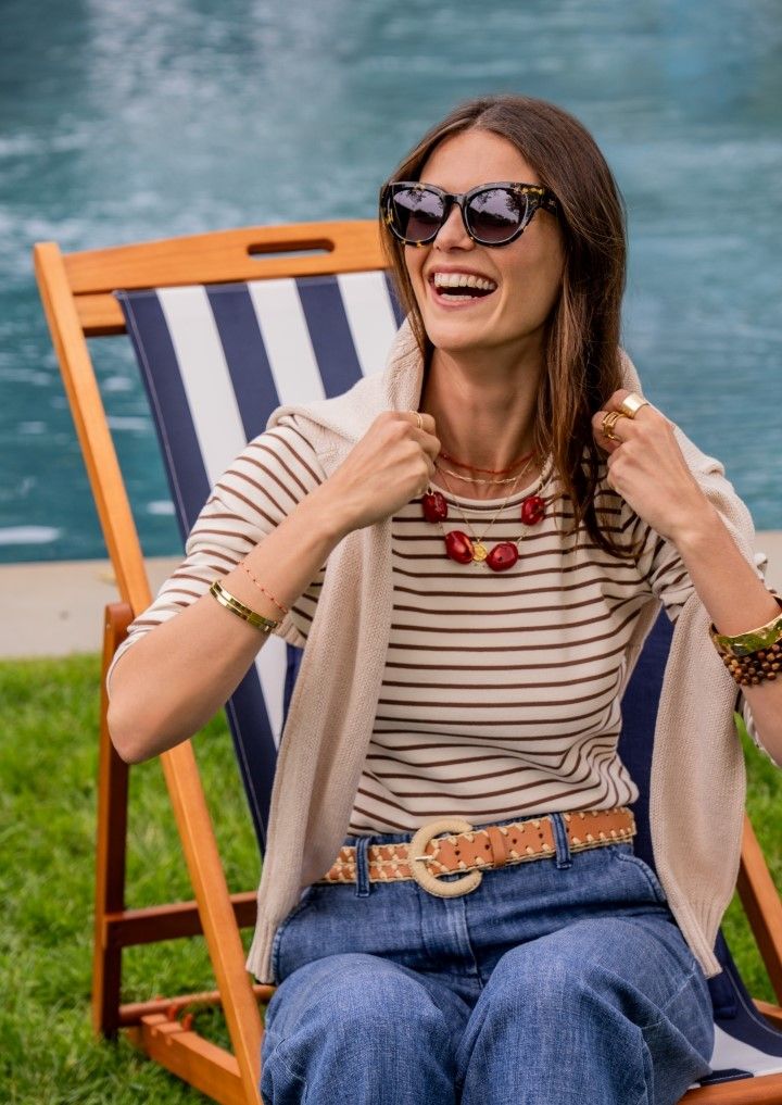 woman sitting in blue and white stripe lawn chair wearing brown stripe knit top