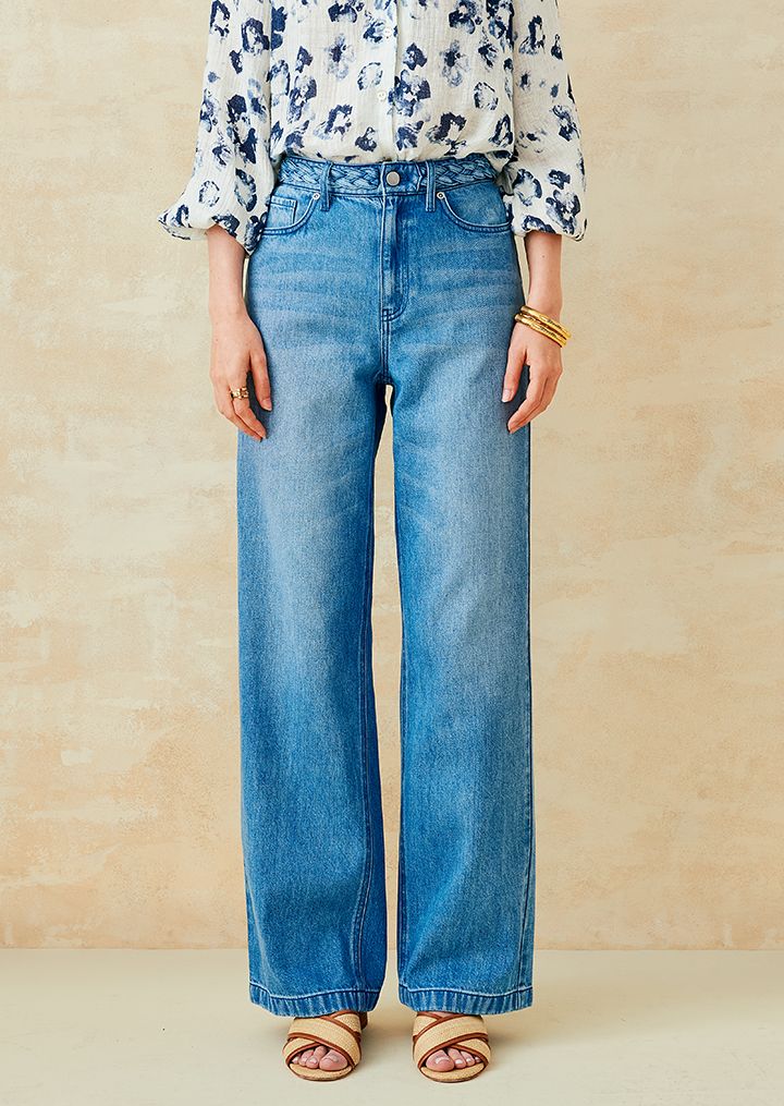 Woman standing in blue jeans with a braided waist. 