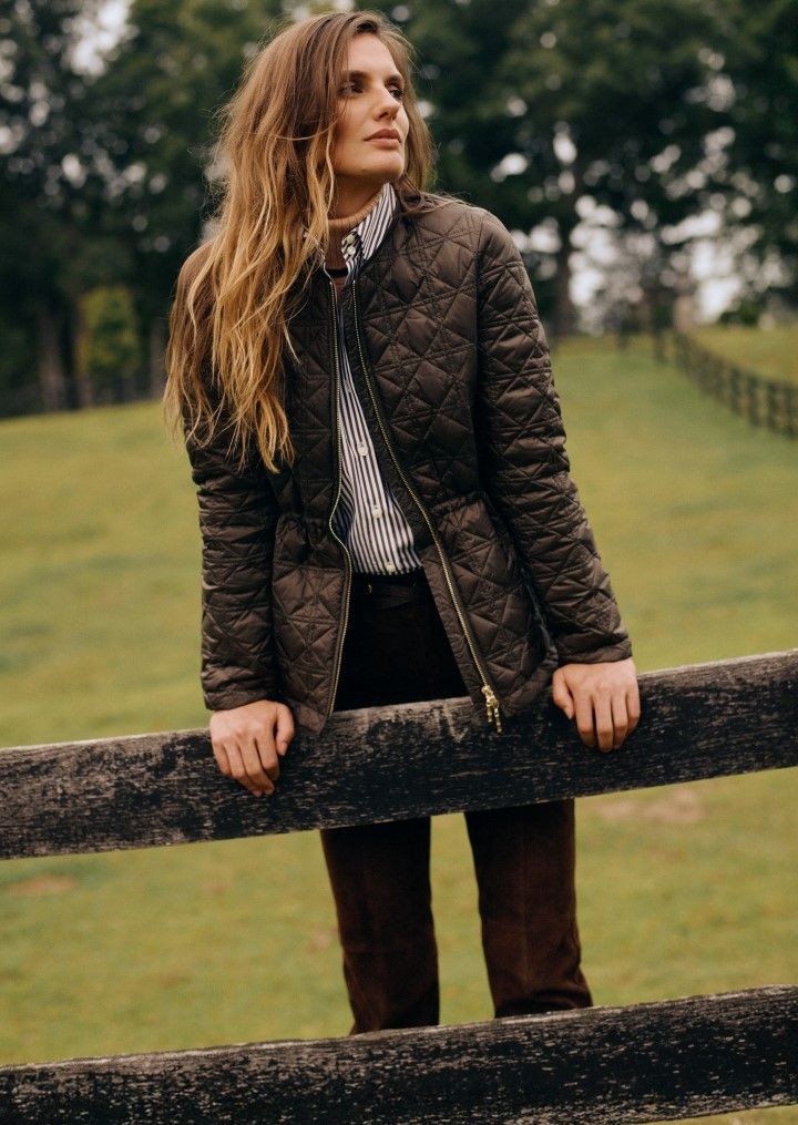 woman leaning on fence wearing olive quilted jacket
