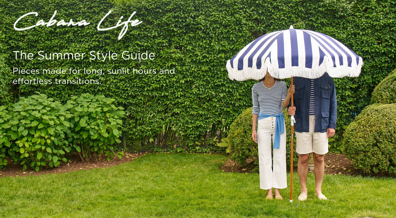 man and woman standing outside in navy and white outfits holding a blue and white stripe umbrella