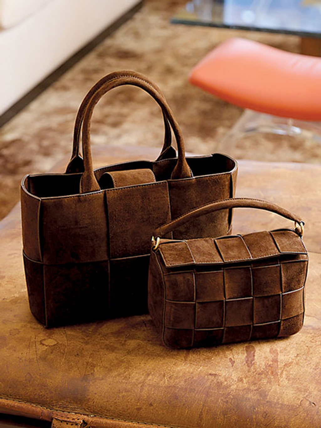 A larger woven tote and a smaller woven top-handle bag on an ottoman A larger woven tote and a smaller woven top-handle bag on an ottoman