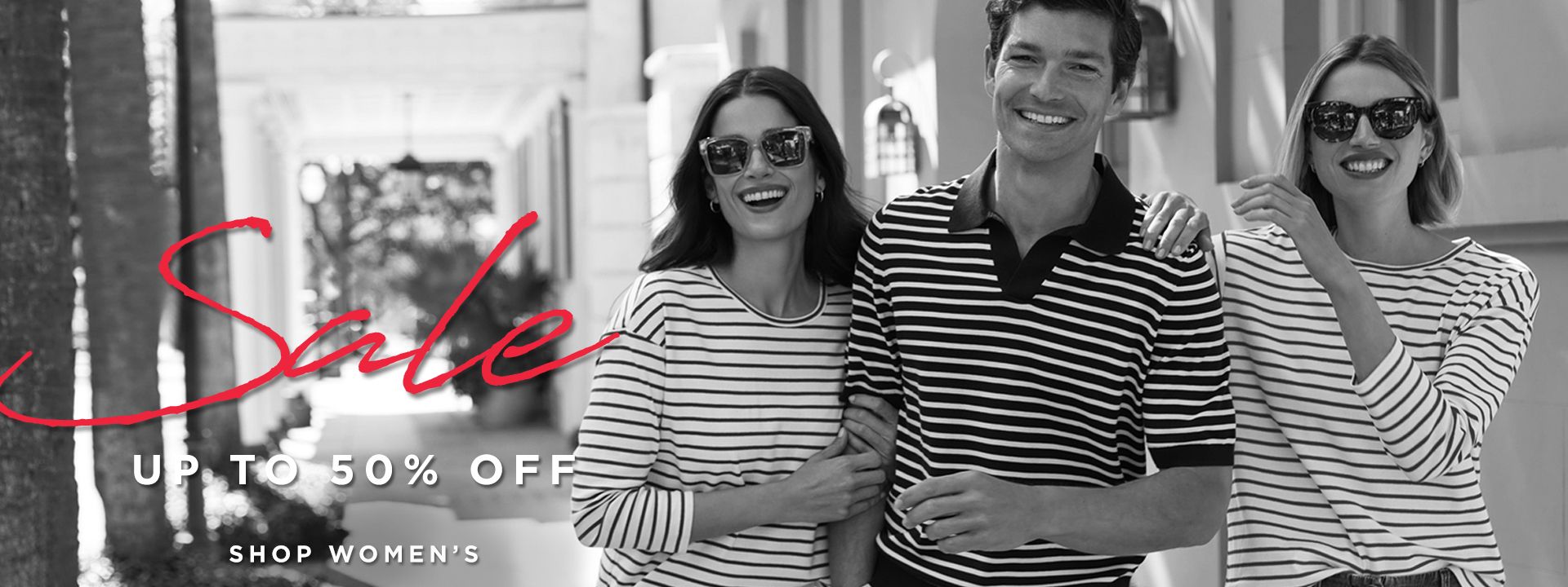 Three smiling models wearing striped tops stand arm-in-arm outdoors, promoting a fashion sale. Text overlaid reads 'Sale - Up to 50% Off' with links to 'Shop Women's' and 'Shop Men's.'