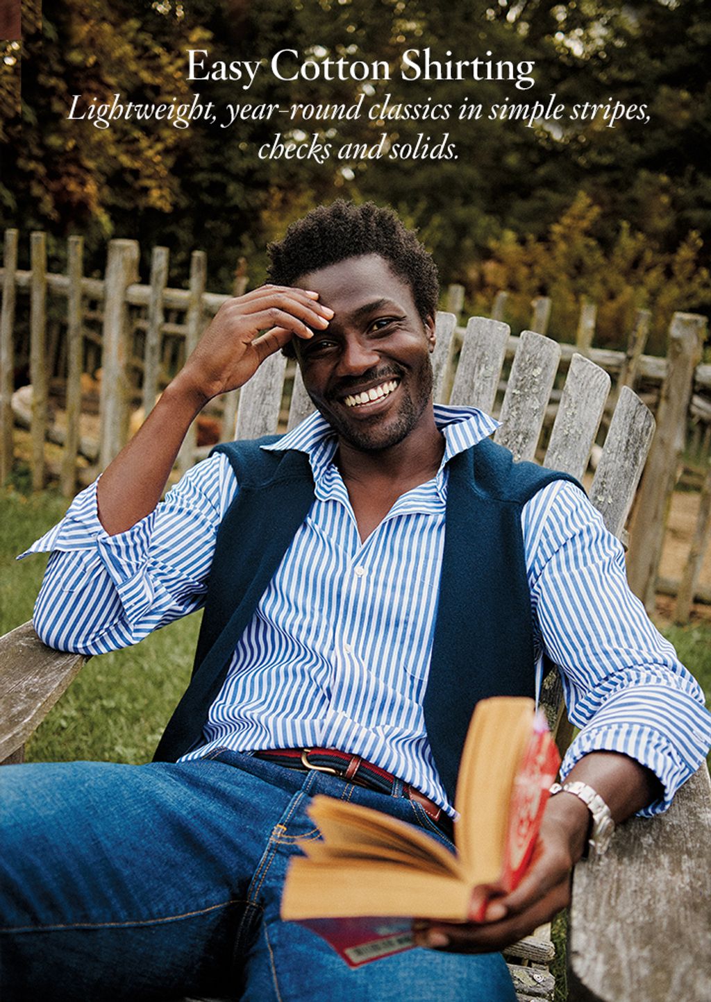 Male seated outside wearing a blue and white striped button down shirt and jeans.