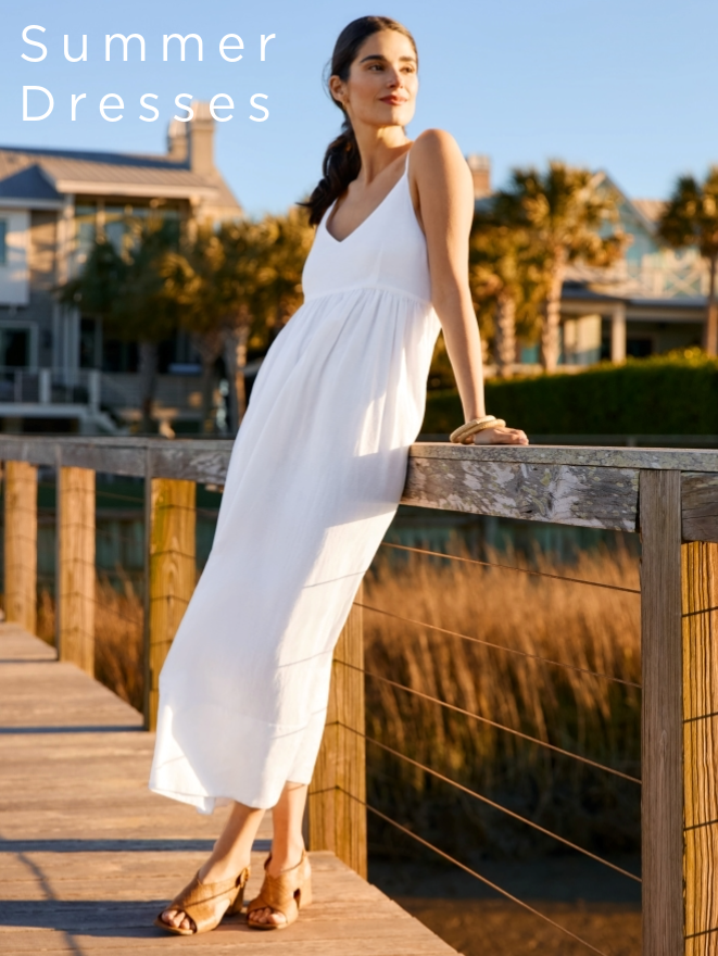 woman standing on a pier wearing a white spaghetti strap flowy midi dress