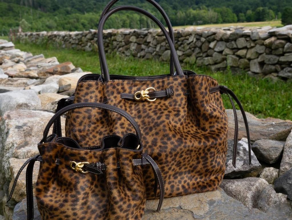 Two leopard print handbags with gold clasps and brown leather straps on a stone wall.