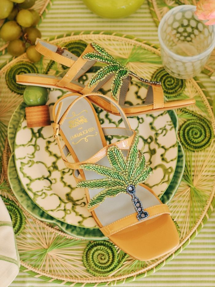 laydown of womens t strap heels with palm tree sequin embroidery positioned on green theme table top