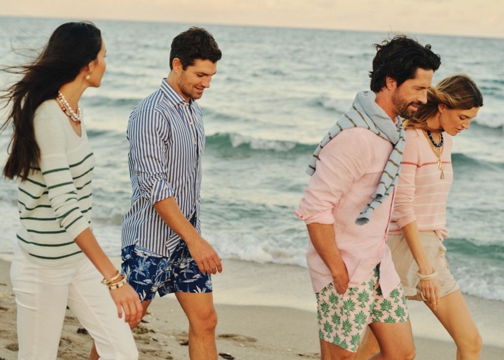 Four casually dressed people walk along a sandy beach beside the ocean.