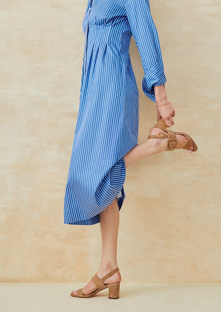 Woman holding her heel wearing a blue and white striped dress. 