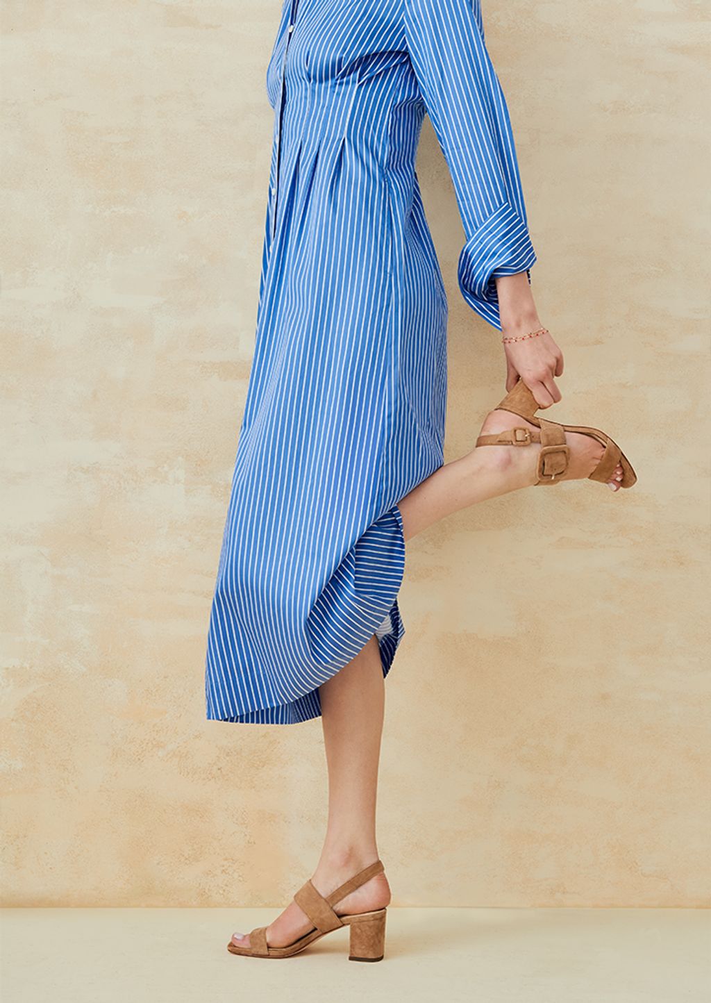 Woman holding her heel wearing a blue and white striped dress. 