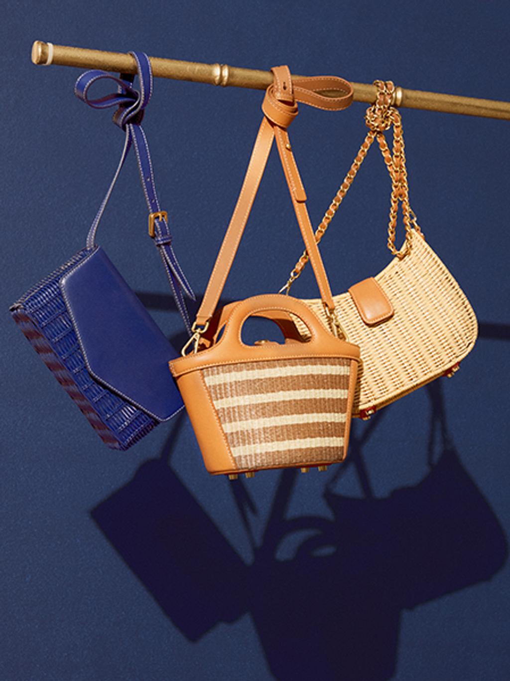 A dark blue handbag, a striped brown handbag, and at an wicker handbag posed hanging off a brown pole