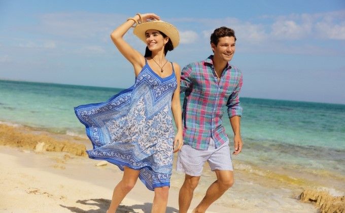 woman on a beach wearing a sleeveless silk paisley printed knee length hankerchief style dress and straw hat