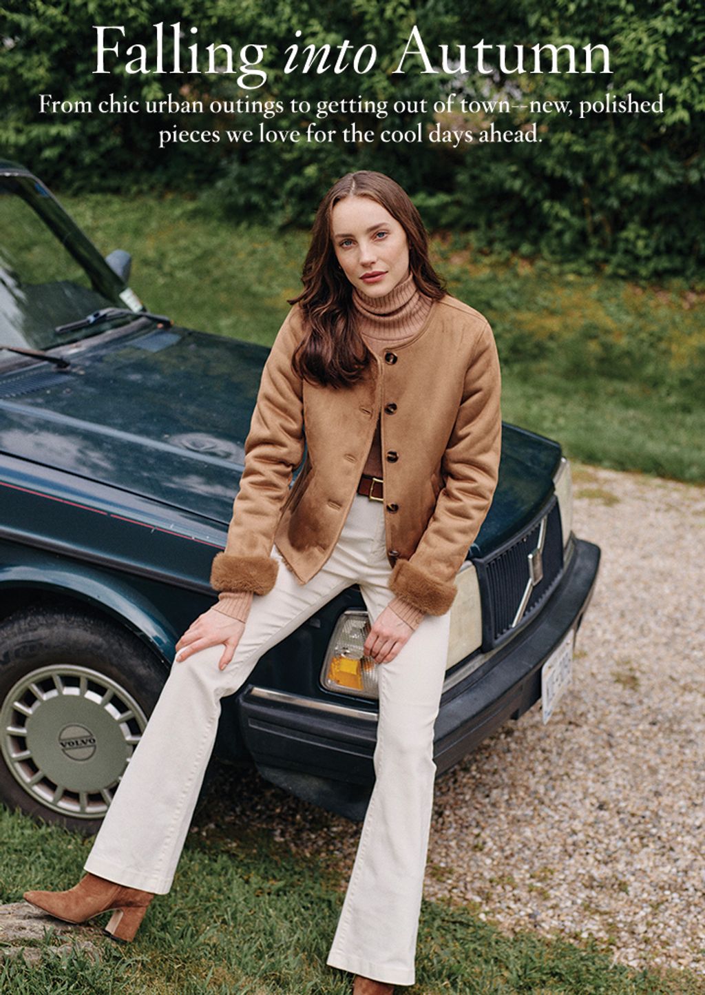 Woman sitting on hood of car in white jeans and camel jacket
