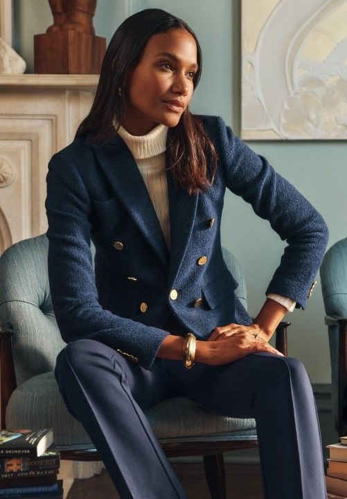 woman seated inside on armchair wearing navy double breasted boucle blazer