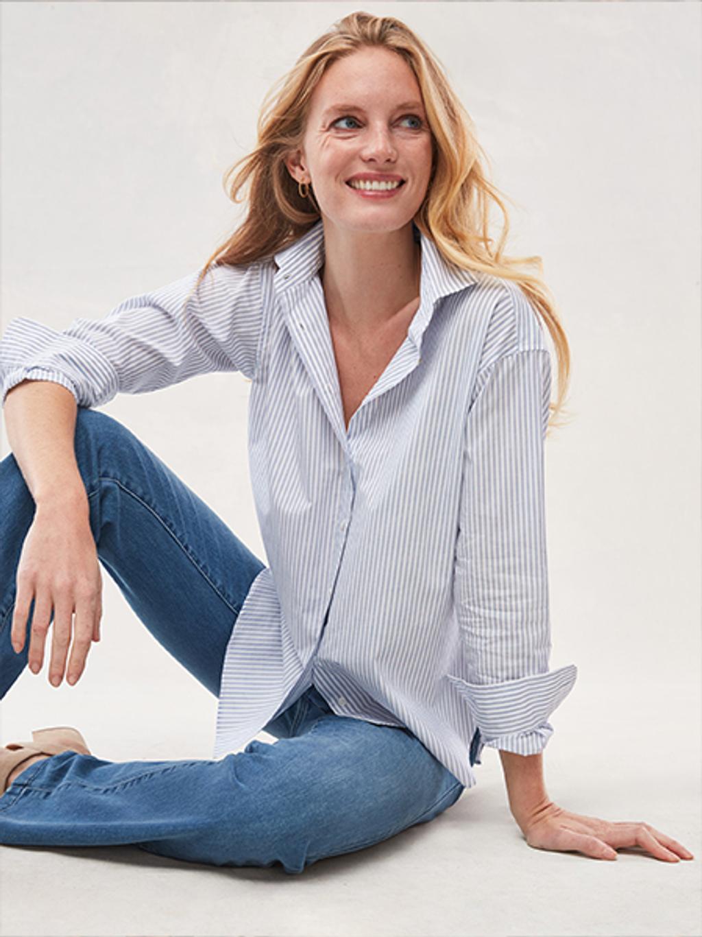 Women with blonde hair smiling, wearing a light blue and white striped button down shirt and blue jeans.