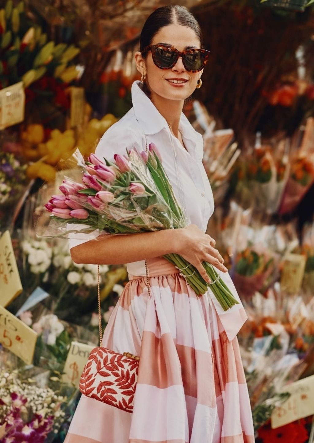 woman standing outside holding a bouquet of flowers and wearing a white button down shirt and a pink and white oversize gingham silk taffeta ball skirt